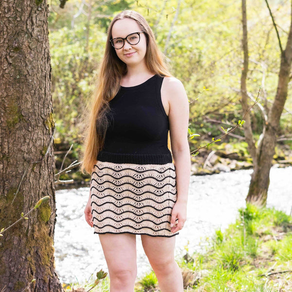 Frau mit Brille steht neben einem Baum und trägt einen selbst gestrickten Rock mit einem sommerlichen Muster der aus Baumwollgarn von Lang Yarns gestrickt wurde. 